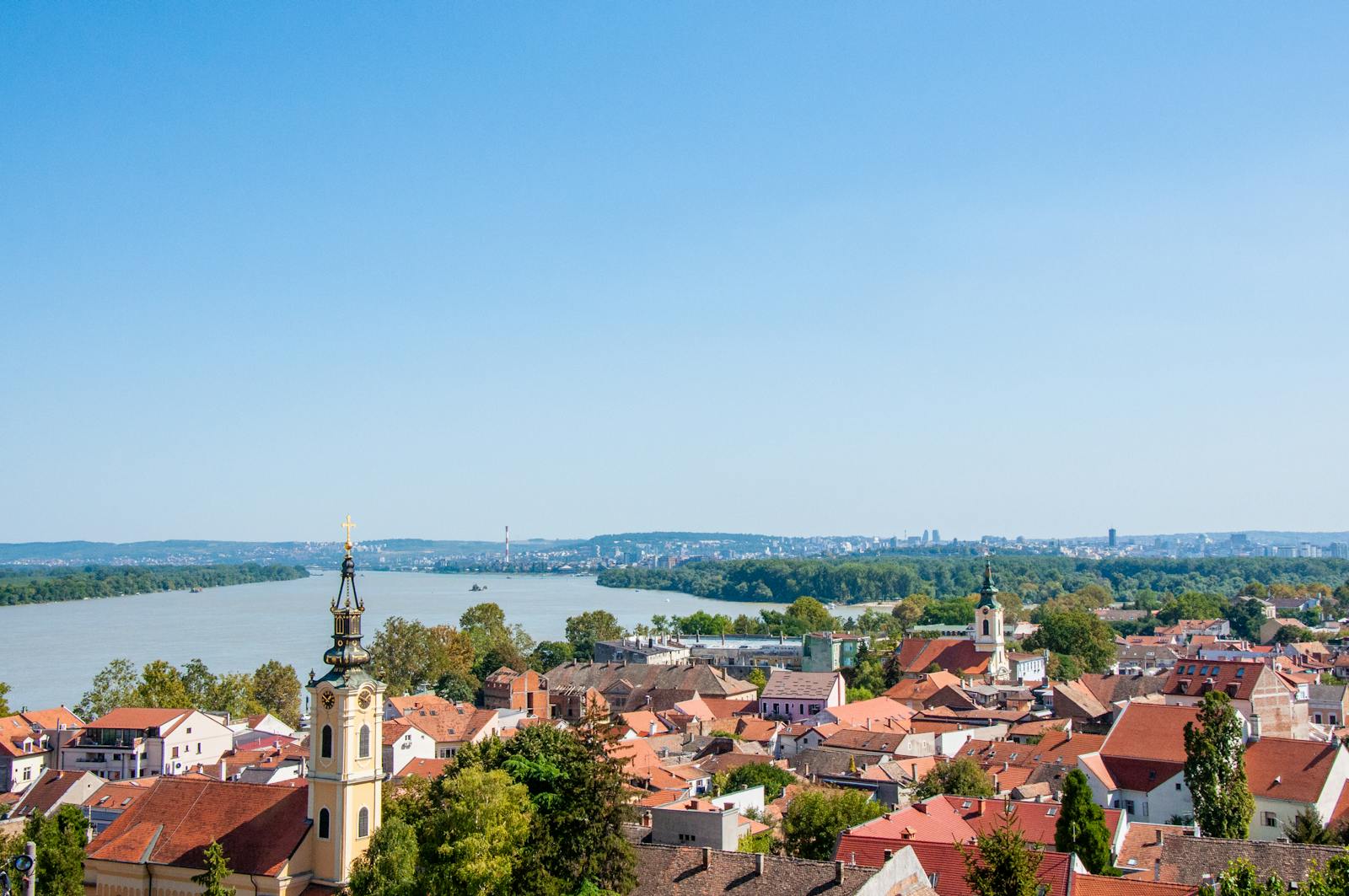 A picturesque aerial view of Belgrade, Serbia with rooftops and a river under a clear summer sky.